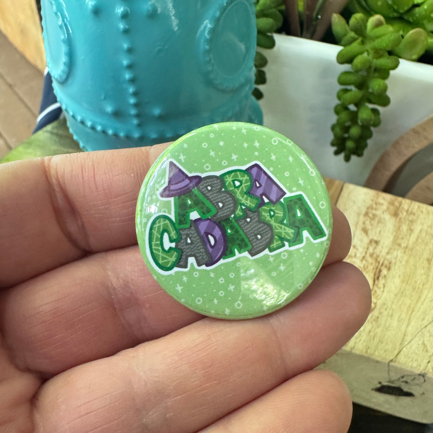 Hand holding a round green button with a design near a wooden surface