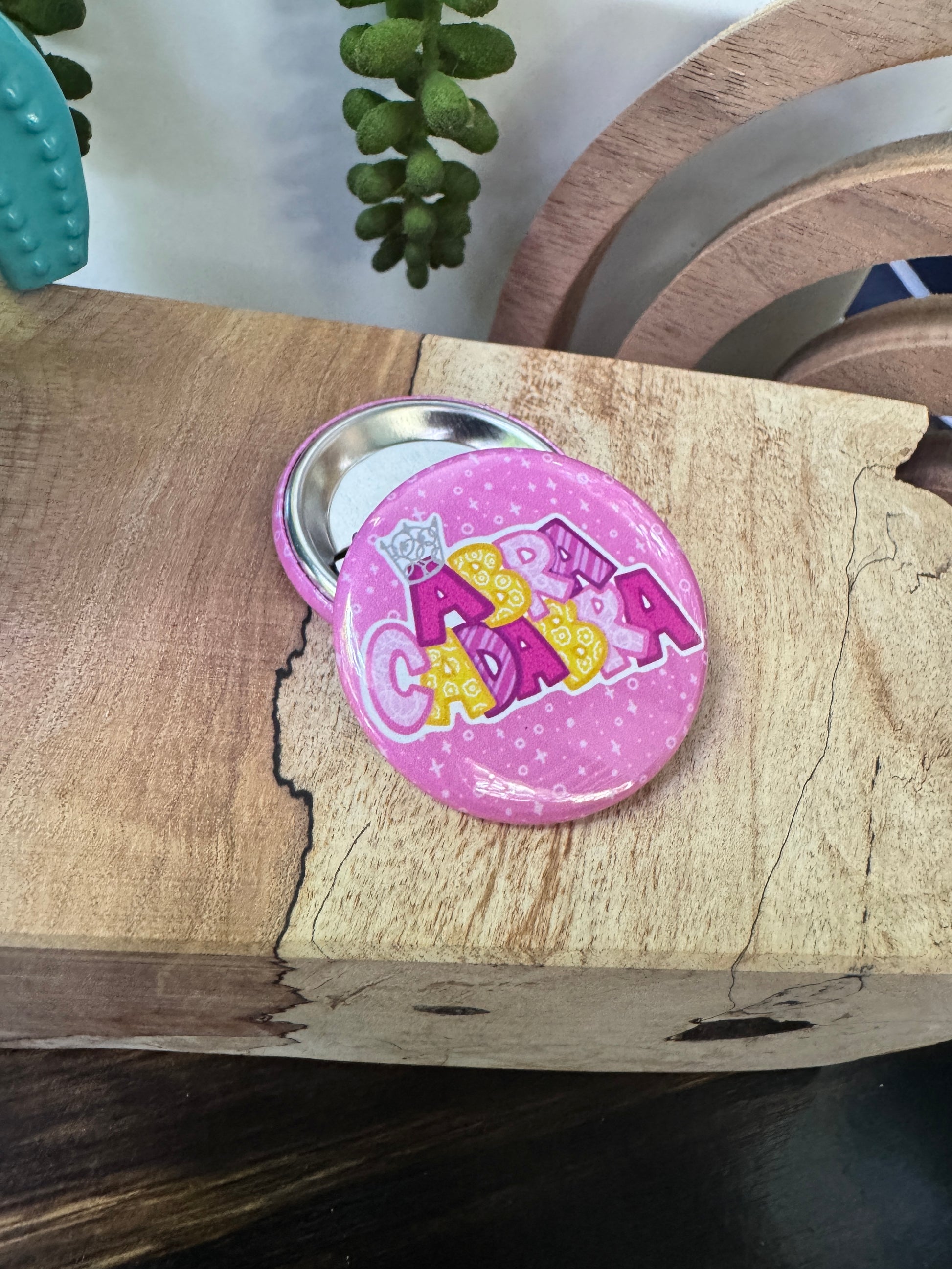 Pink button with yellow and pink text on a wooden surface